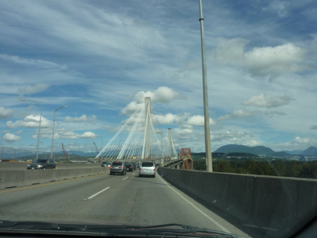 Photo of bridge with dramatic span, and cars crossing the bridge. Mountains in the background.