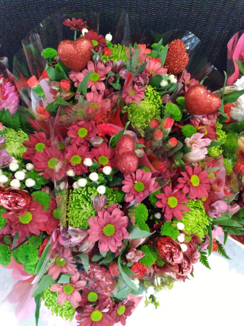 First photo is of a fancy heart-shaped box of chocolates; second photo is of a Valentine's Day bouquet with tiny white mums, green-centered red daisies and green mums plus sparkly red hearts. 