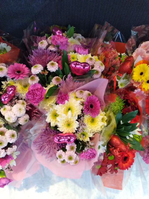 Photo of a Valentine's Day bouquet with a mixture of mostly pink flowers but some red and one yellow. Flowers are mostly mums. 